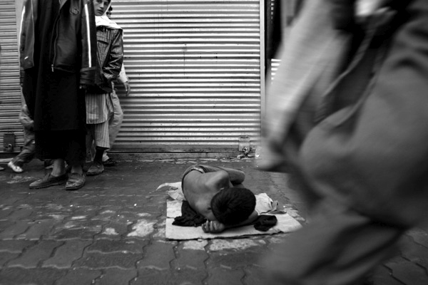A young boy lays down begging on a busy street in Kabul, Afghanistan.  Due to years of conflict in Afghanistan, thousands of children have been orphaned, with no one to take care of them they beg on the streets or work menial jobs.  October 2006.