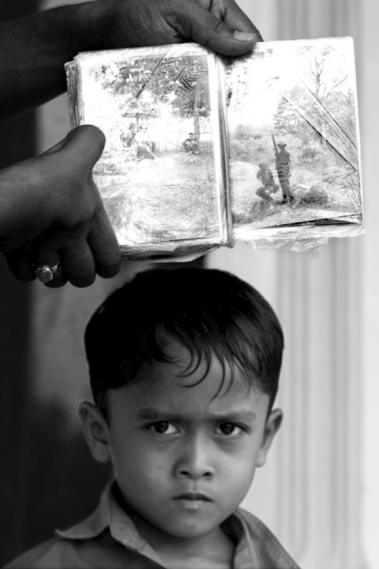 The son of Mukhlis Basyar, a Free Aceh Movement commander, looks on as his father shows photos taken while in the jungles of Aceh.  To date the peace accords signed between GAM and the Indonesian army after the devastating tsunami, which killed an estimated 300,000 people, still holds.  February 2007.