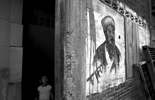 A young girl peers around the corner at the painting her brother did of Osama Bin Ladin on the wall of their home, in Banda Aceh, Indonesia.  February 2007.