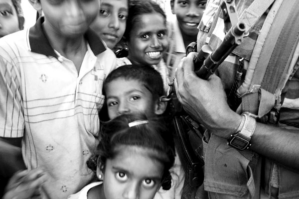 Children play around Sri Lankan army guards while waiting to be transferred to a new internally displacement camp one month after the tsunami in Batticaloa, Sri Lanka.  This area is Tamil Tiger controlled and received very little of aid promised by the donors or government.  February 2005.