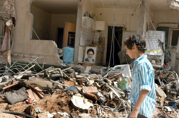 17 August 2006, Lebanon, Beirut, Dahia . 2006 Lebanon War. Unidentified young boy walks by breakage and that the background a picture of Ayatullah Khomeini, Iran's political and religious leader till his death. 